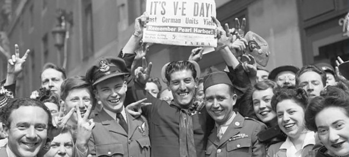 Image of crowds Celebrating VE Day in the UK holding up newspaper