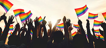 Celebrating pride month - image shows hands raised in celebration with many pride flags held aloft