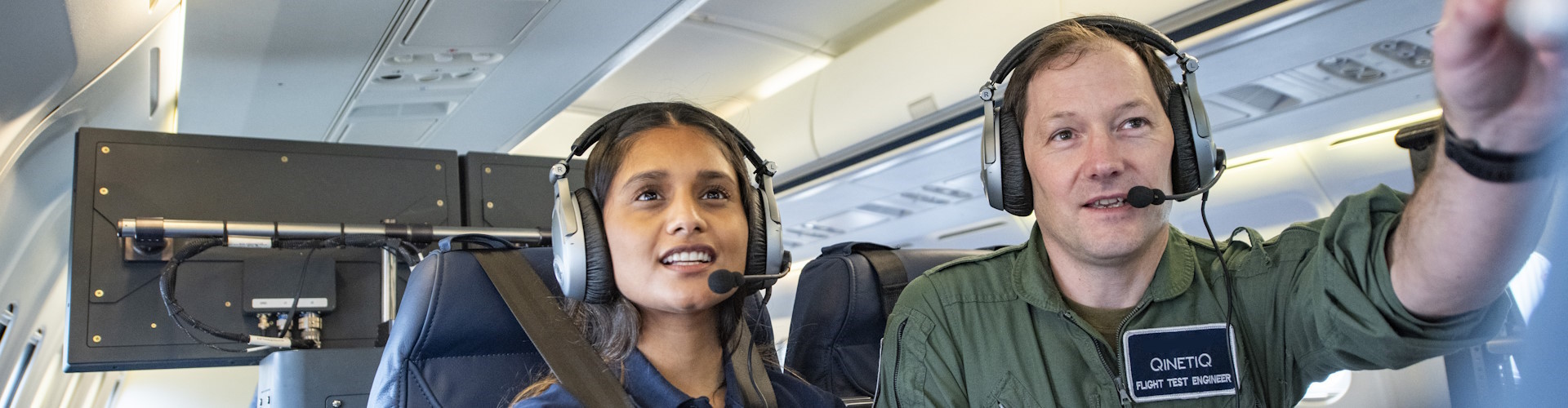 A Flight Test Engineer and another QinetiQ employee sat on an aircraft, analysing data on a computer.
